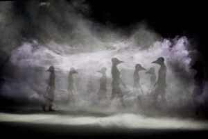 Scène de Poussières baignée dans la brume, où des personnages à tête de corbeau émergent de la fumée.